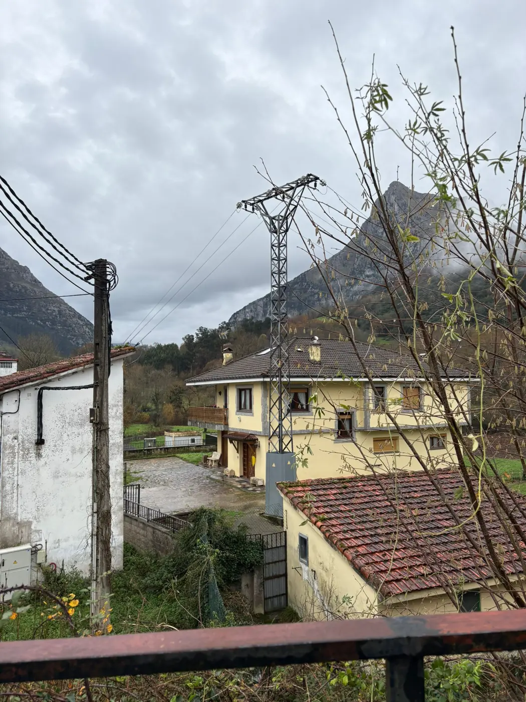 Línea eléctrica aérea con apoyo metálico junto a viviendas en un entorno rural de montaña